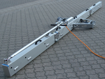 Balkenförmiges graues Messgerät mit zwei seitlich angeordneten Rädern mit Kabel auf Verbundpflaster