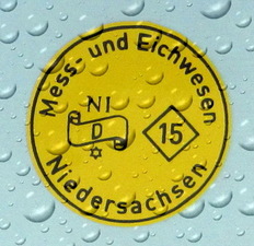 Detailaufnahme einer gelben, mit Wassertropfen überzogenen Eichmarke des Mess– und Eichwesen Niedersachsen für das Jahr 2015