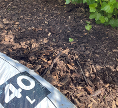 Auf der rechten Seite liegt ein Sack mit der Aufschrift 40 Liter auf braunem Rindenmulch