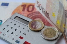 auf einem silbernen Taschenrechner liegen Euromünzen und dahinter liegen Geldscheine