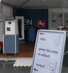Blick ins Zelt und Vitrine beim Tag der Niedersachsen 2026 mit weißem Blitzerfotogerät auf grauer Kiste.