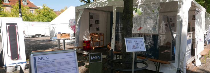 Weißes Pavillonzelt mit MEN-Aufsteller und MEN-Tafel auf Ausstellungsfläche