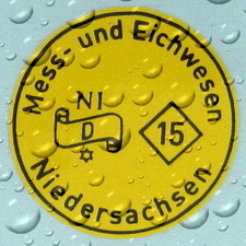 Detailaufnahme einer gelben, mit Wassertropfen überzogenen Eichmarke des Mess– und Eichwesen Niedersachsen für das Jahr 2015