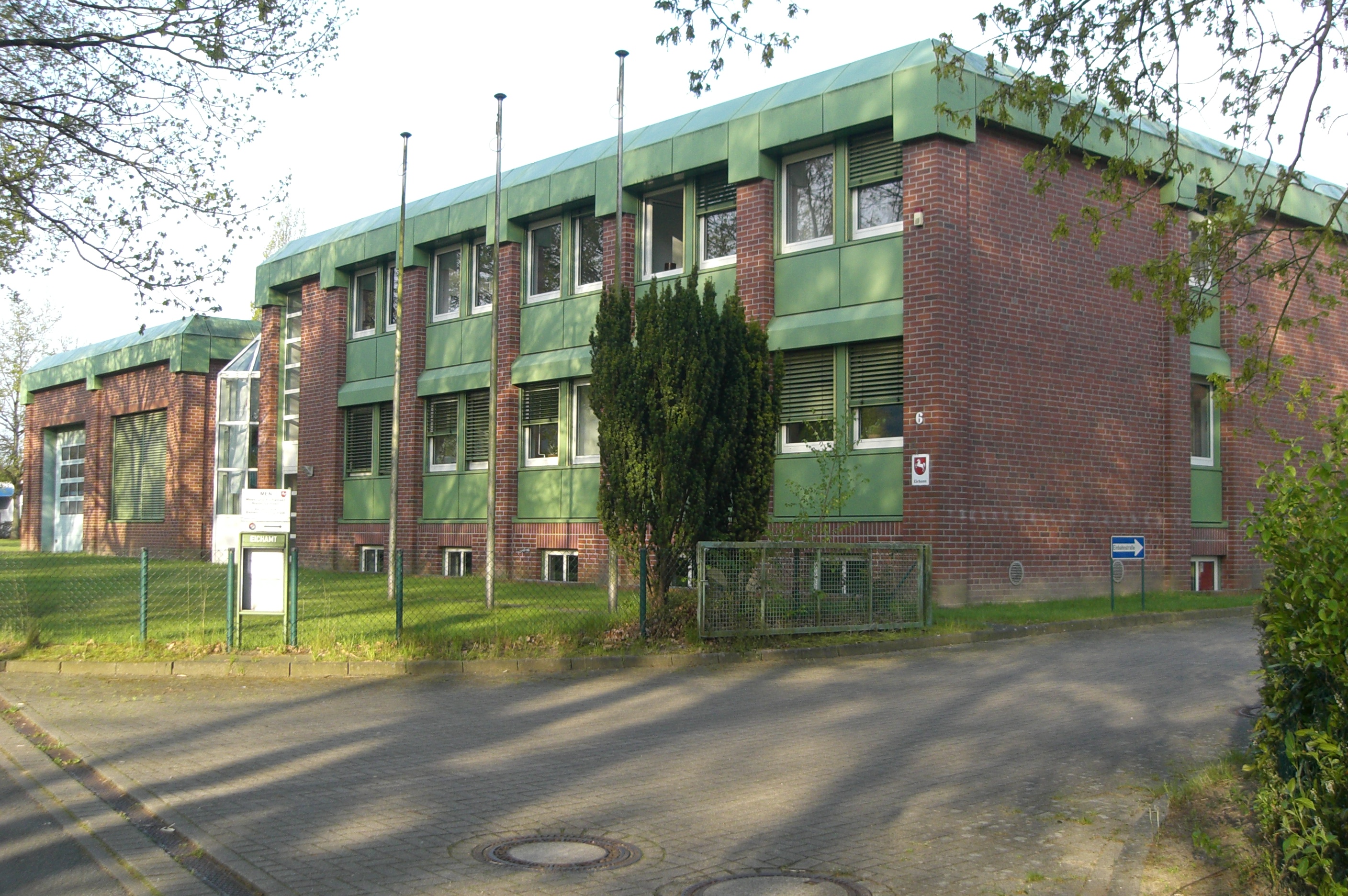 Seitenansicht des zweigeschossigen Gebäudes der Betriebsstelle des Mess- und Eichwesen Niedersachsen in Stade aus rotem Backstein mit grünem Flachdach und grünen Fensterumrahmungen